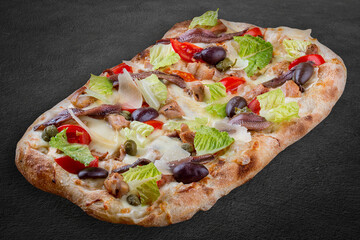 Caesar pizza with chicken, anchovies, romaine, cherry, kalamata, capers, pesto. Roman pizza rectangular on dark background