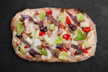Caesar pizza with chicken, anchovies, romaine, cherry, kalamata, capers, pesto. Roman pizza rectangular on dark background