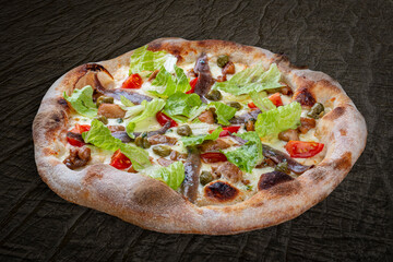 Caesar pizza with chicken, anchovies, romaine, cherry, kalamata, capers, pesto. Neapolitan round pizza on wood background