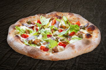 Caesar pizza with chicken, anchovies, romaine, cherry, kalamata, capers, pesto. Neapolitan round pizza on wood background