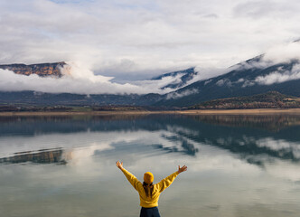View from behind of woman spreading her arms excited about the beautiful scenery of the calm lake where the mountains are reflected