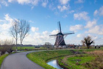 Countryside landscape view of traditional Dutch windmill under blue sky in winter, Polder and water land, Small canal, ditch or river on the grass field along Gein river, Abcoude, Utrecht Netherlands
