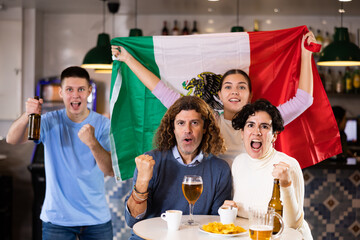 Group of friends, excited supporters cheering for favorite team with flag of Mexico while watching...