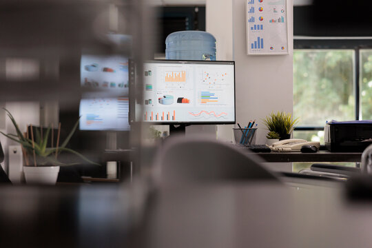 Empty Startup Office With Desktop Computer Showing Corporate Software Management With Growth Graphs And Statistics On The Screen On The Desktop. Workplace With No People Working In It.