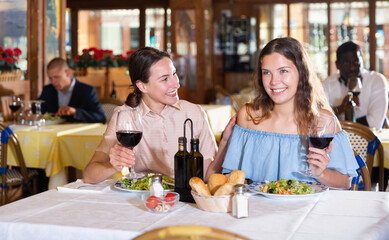 Two young female friends smiling at dinner in a restaurant, celebrating something