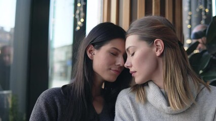 Gay female couple have postive expressions, sit close to each other at cafeteria, laughing joyfully. Lesbians couple and love concept