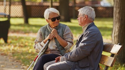 Naklejka na ściany i meble Blind older woman with her husband sitting on a bench in the park. High quality photo