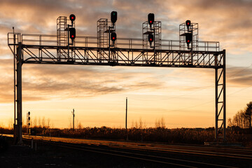 A railway light signal bridge is silhouetted by the setting sun