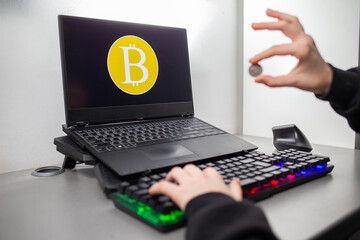 Palce trzymające monetę w tle widać znak bitcoina. Bitcoin między palcami. Fingers holding a coin in the background you can see the bitcoin sign. Bitcoin between your fingers. Bitcoin na komputerze.
