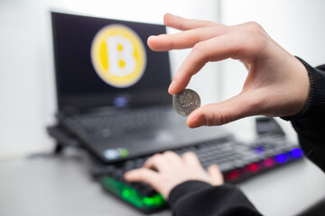 Palce trzymające monetę w tle widać znak bitcoina. Bitcoin między palcami. Fingers holding a...