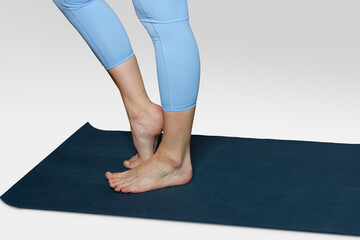 Women's legs in blue yoga pants stand on a gymnastic mat on a toe.