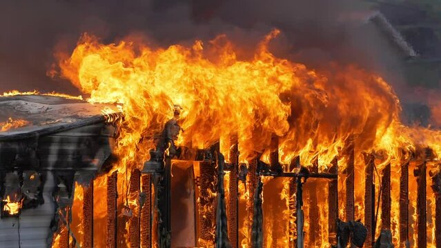 Small home engulfed in flames with a large fire. Slow motion footage of large flames. Fire and smoke billowing out of a trailer home.