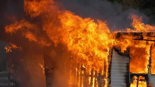 Intense house fire burns a trailer home until there is nothing left. Close up slow motion shot of huge flames engulfing a small building.