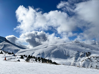 ski slopes of a winter resort, on a blue sky day with big cotton clouds behind the mountains,...