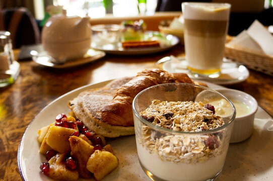 Breakfast served with coffee, granola, croissant, pancakes, and fruits. Healthy and delicious cafe morning meal concept.