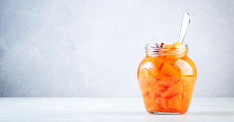 Quince jam or confiture in glass jar with cinnamon and anise on gray kitchen table background, copy space banner