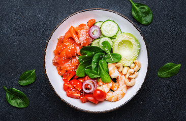 Ketogenic diet salad bowl with salmon, shrimp, avocado, spinach, cucumber, tomato, cashew nuts, sesame. Low-carbohydrate breakfast rich in healthy fats. Black table background, top view
