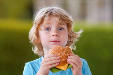 A blond boy enjoys eating a cheeseburger