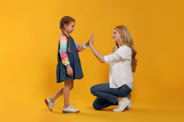 Mother and daughter giving high five on orange background