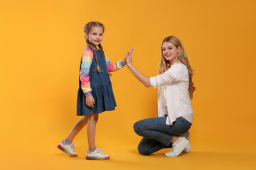 Naklejka premium Mother and daughter giving high five on orange background