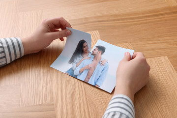 Woman ripping photo at wooden table, closeup. Divorce concept