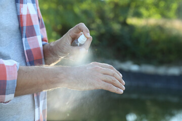 Man applying insect repellent onto hand outdoors, closeup