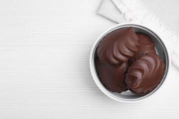Delicious chocolate covered zephyrs in bowl on white wooden table, top view. Space for text