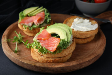 Tasty rusks with salmon, cream cheese and avocado served on black table, closeup