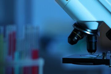 Closeup view of modern microscope with glass slide on blurred background, toned in blue. Space for text