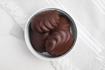 Delicious chocolate covered zephyrs in bowl on white wooden table, top view
