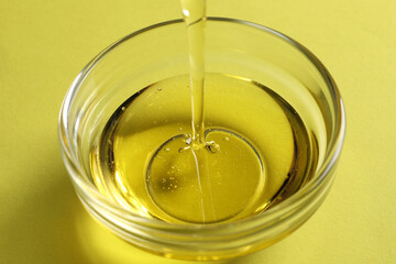 Pouring cooking oil into bowl on yellow background, closeup