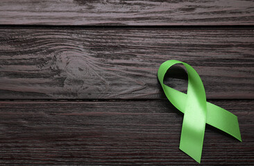 World Mental Health Day. Green ribbon on wooden background, top view with space for text