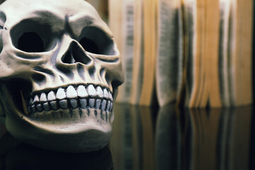 Human skull and old book on mirror table, closeup. Space for text