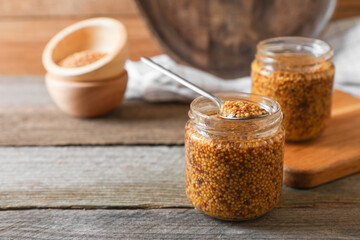 Jars and spoon of whole grain mustard on wooden table. Space for text