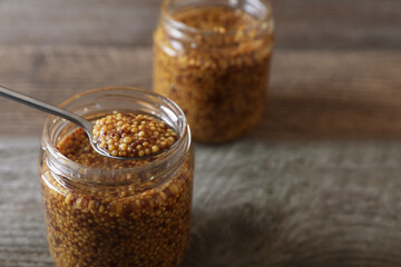 Jars and spoon of whole grain mustard on wooden table, closeup. Space for text