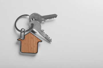 Keys with trinket in shape of house on white background, top view and space for text. Real estate agent services