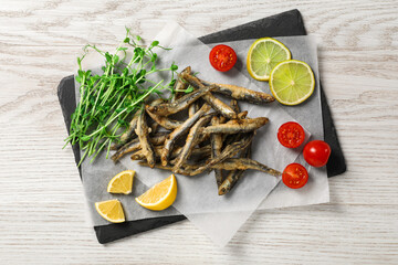 Slate board with delicious fried anchovies, lime and tomatoes on white wooden table, top view