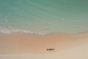 Drone view of girl and her shadow playing at a crystal clear beach