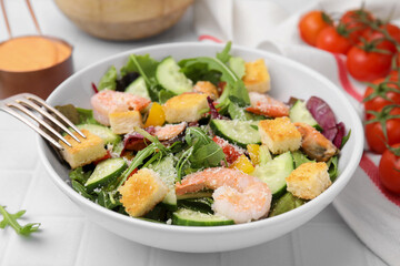 Delicious salad with croutons, cucumber and shrimp served on white tiled table, closeup