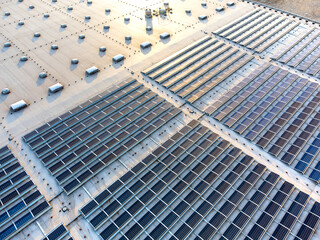 Large solar panel array farm on a commercial warehouse building in sunset aerial view