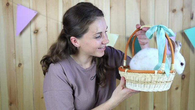 Cute white rabbit in a wicker basket in the hands of a young woman