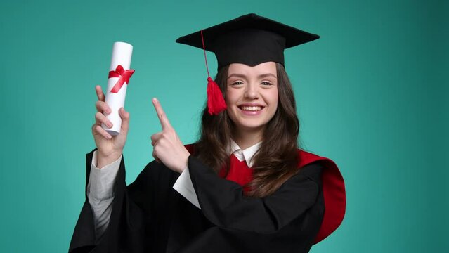 Portrait of a proud student achieving her goal. Close-up view of a cheerful female bachelor in a hat and gown kissing her diploma. High quality 4k footage