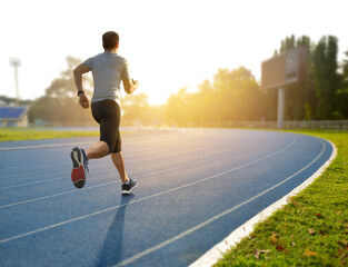 A man running on athletic track with sunrise background...