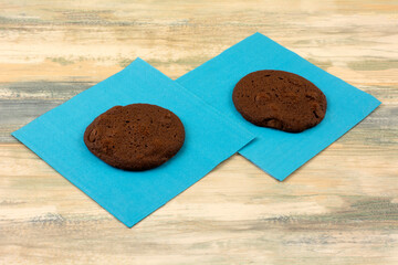 Two  chocolate cookies with chocolate chips on blue snack napkins