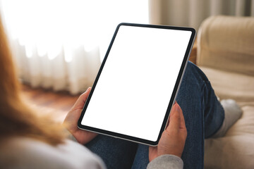 Mockup image of a woman holding digital tablet with blank desktop screen while lying on a sofa at home