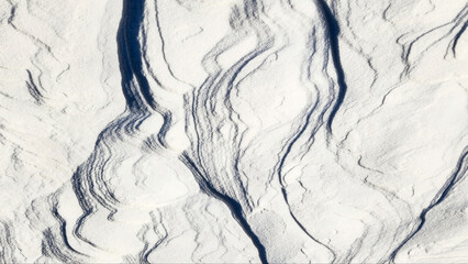 Snow top view. The texture of the snow crust. Winter light background in a blue shade. The play of light and shadow on the undulating slopes of snow drifts. Selective focus.