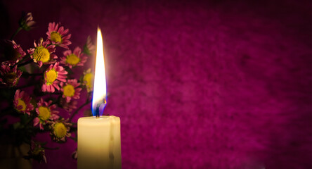 Close up of yellow wax candle flame and flowers