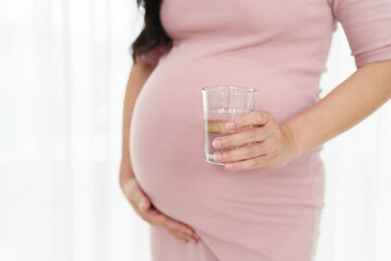 close up pregnant woman drinking water on window background