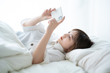 ベッドの上でスマートフォンを操作する女性 