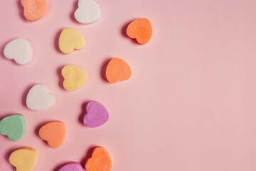 Colorful heart shaped sugar candies on pastel pink background